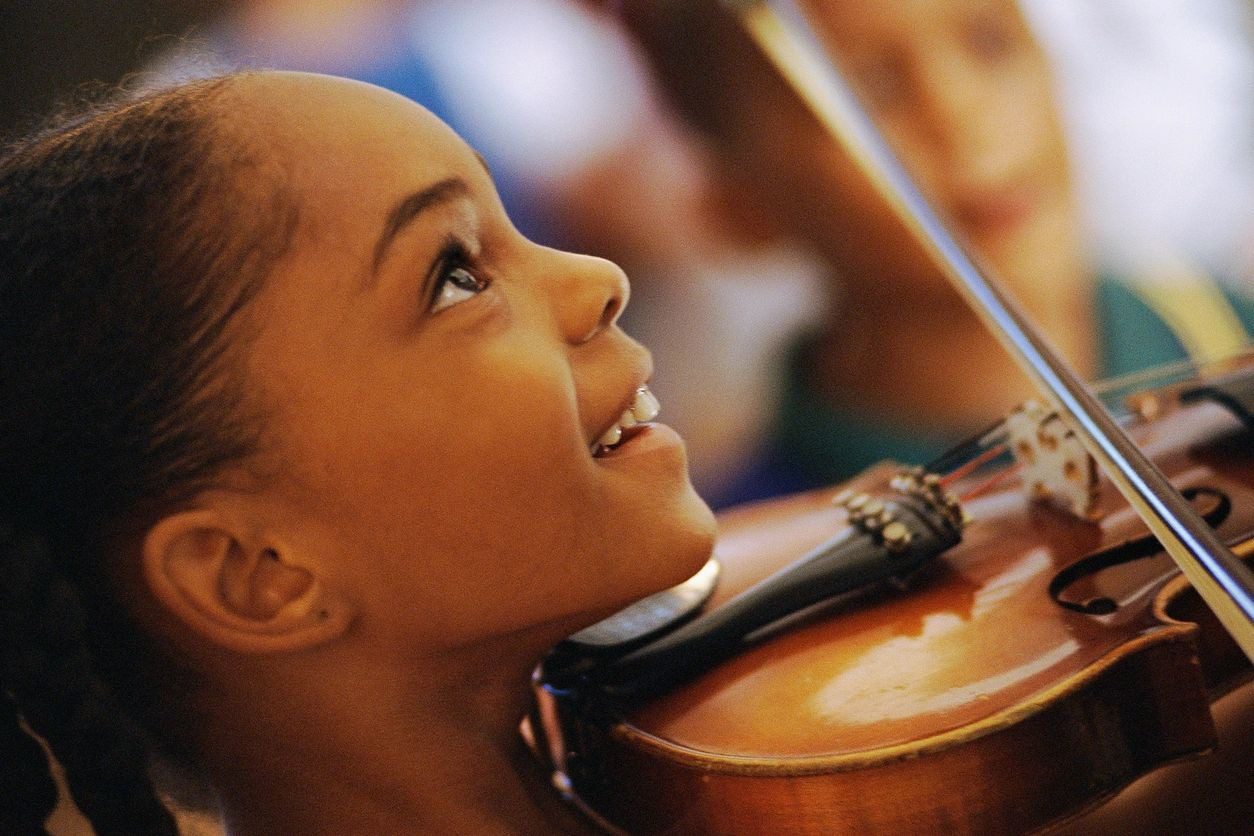 Young girl smiling while playing violin.